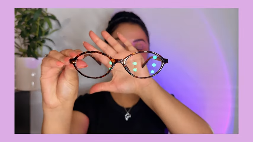 Kirsty Noskcaj holds up the Andrea blue light - blocking glasses, showcasing their round tortoiseshell design with cute gold accents.