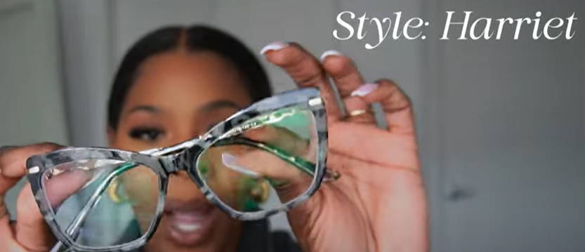 Tara Shanice holding Lensmart Harriat black tortoise frames (Style: Harriet), featuring cat - eye - like design with green specks and gold accents.