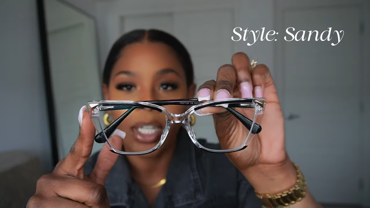 Tara Shanice holding Lensmart Sandy frames – transparent design with black rims, perfect for versatile everyday elegance.