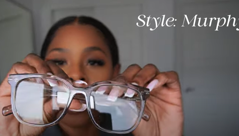 Tara Shanice holding Lensmart Murphy frames, dark transparent acetate with double - line detailing, ideal for minimalist style.