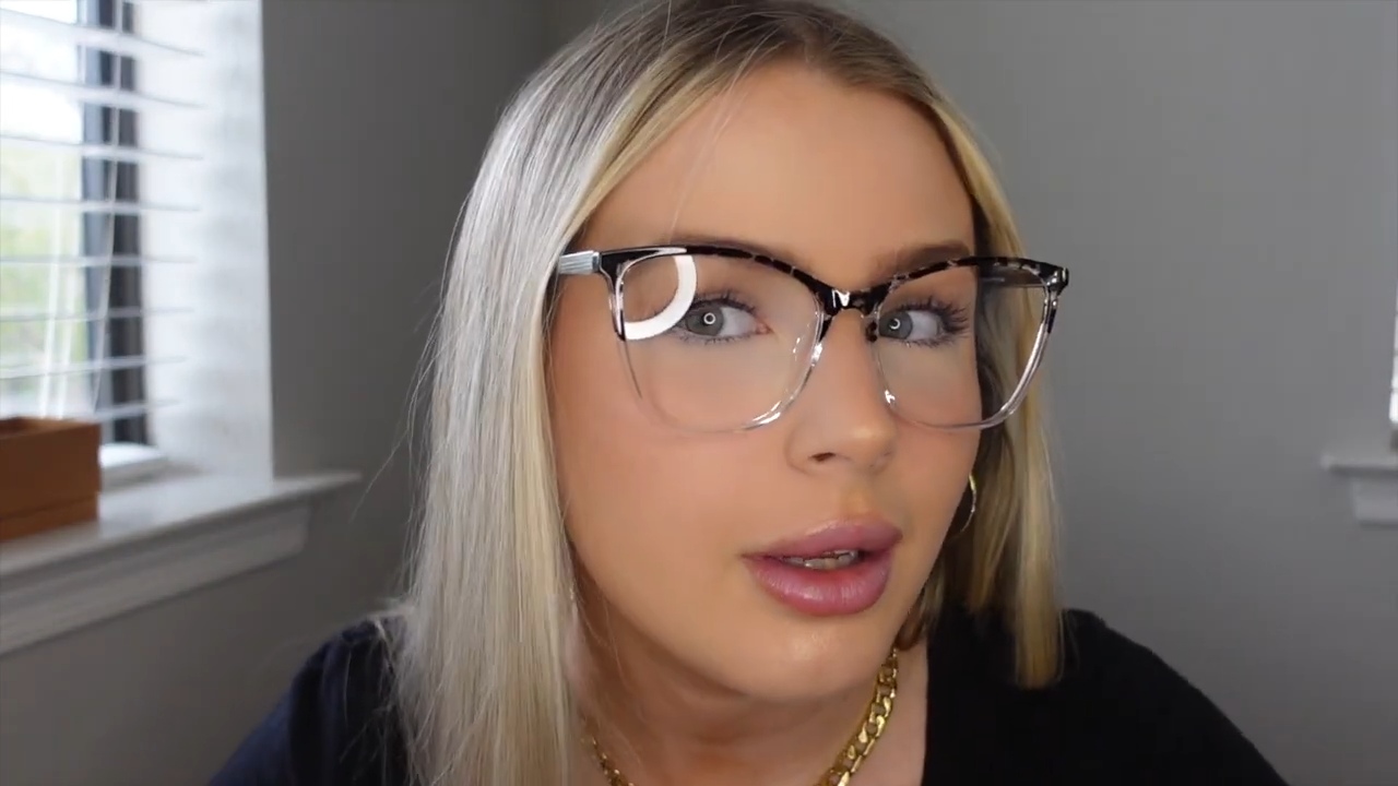 Michaela wearing Ligeia two - tone tortoiseshell glasses, featuring a timeless tortoise pattern on top fading to a crystal - clear finish, lightweight for daily wear, with a velvet carrying case.