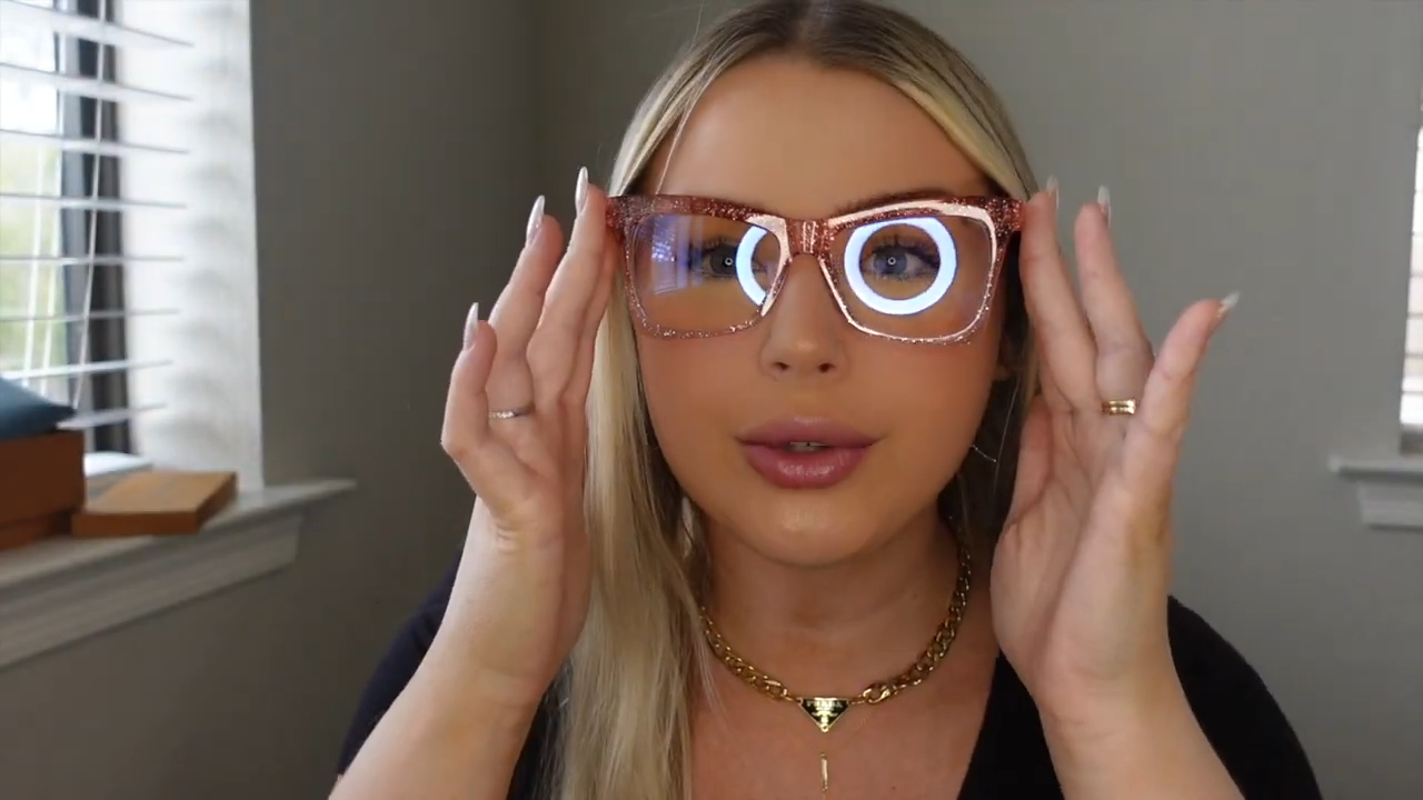 Michaela holding Delphine pink sparkle glasses, featuring vibrant pink hue with embedded sparkles, described as fun, heavy - duty yet lightweight, from Lensmart’s creative prescription collection.